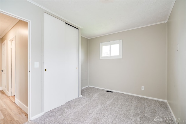 unfurnished bedroom with visible vents, baseboards, light colored carpet, a closet, and ornamental molding