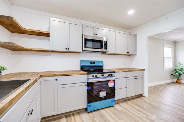 kitchen with light wood-type flooring, butcher block countertops, appliances with stainless steel finishes, open shelves, and ornamental molding
