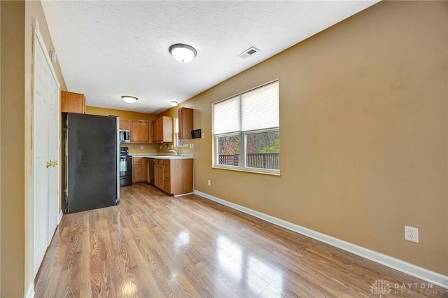 kitchen with freestanding refrigerator, stainless steel microwave, a sink, black range with electric stovetop, and light countertops