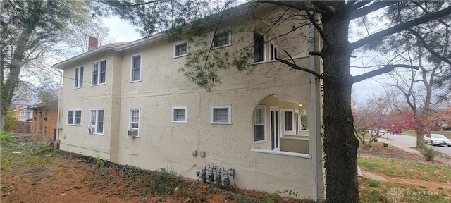view of side of property with stucco siding, cooling unit, and a chimney