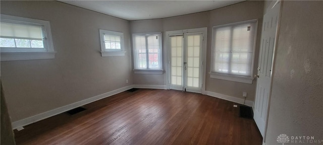 spare room featuring dark wood-type flooring, visible vents, baseboards, and a healthy amount of sunlight