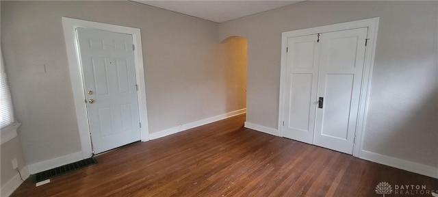 interior space featuring arched walkways, wood finished floors, baseboards, and visible vents