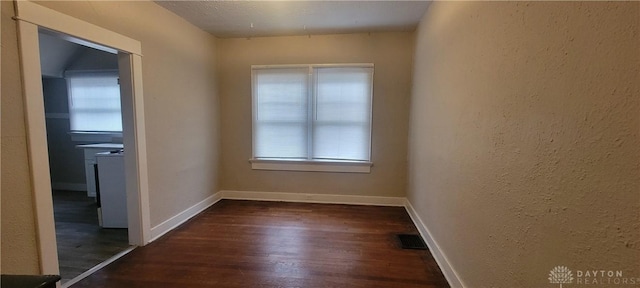 empty room featuring dark wood-type flooring, a textured wall, baseboards, and visible vents