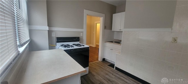 kitchen with dark wood-type flooring, white cabinets, a sink, light countertops, and range with gas stovetop