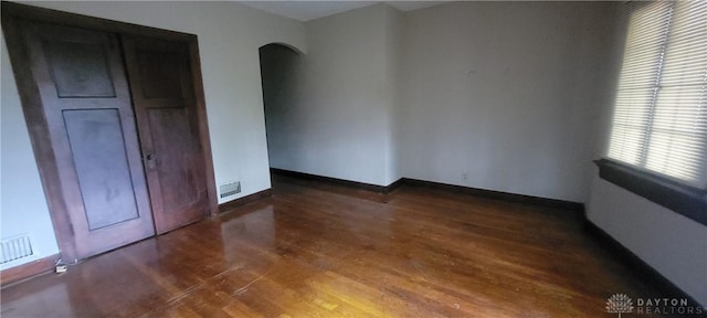 spare room featuring arched walkways, wood finished floors, baseboards, and visible vents