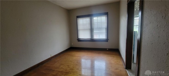 empty room with wood finished floors, a textured wall, and baseboards