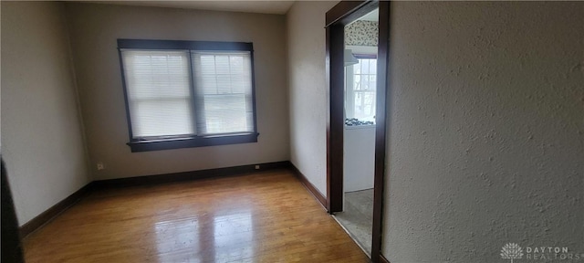 empty room featuring a textured wall, baseboards, and wood finished floors