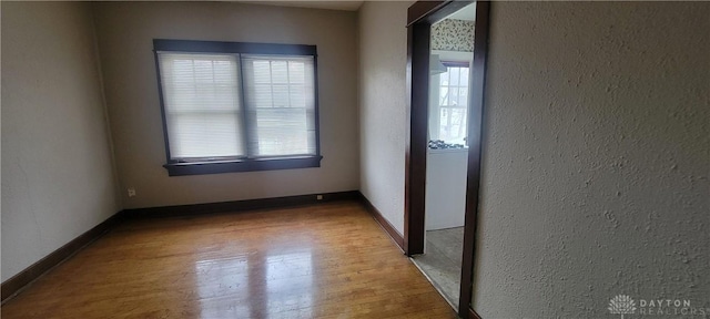 spare room featuring a textured wall, baseboards, and wood finished floors