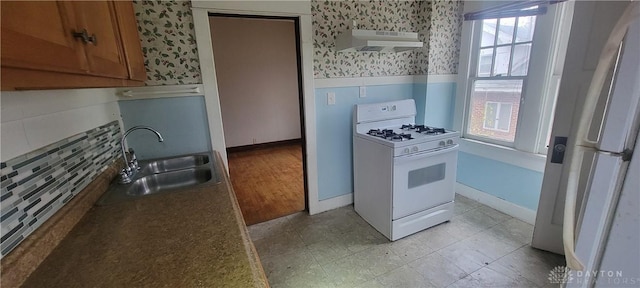 kitchen featuring wallpapered walls, white appliances, a wainscoted wall, under cabinet range hood, and a sink