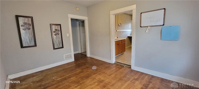 unfurnished bedroom featuring wood finished floors, ensuite bathroom, baseboards, and visible vents