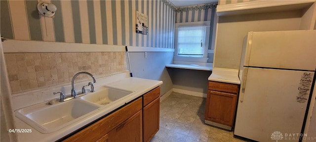 kitchen with brown cabinetry, a sink, freestanding refrigerator, and wallpapered walls