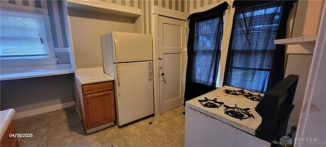 kitchen with brown cabinetry, wallpapered walls, freestanding refrigerator, and light countertops