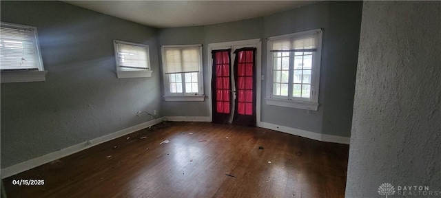 unfurnished room featuring a textured wall, wood-type flooring, and baseboards