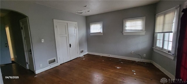 unfurnished bedroom featuring arched walkways, wood finished floors, multiple windows, and visible vents