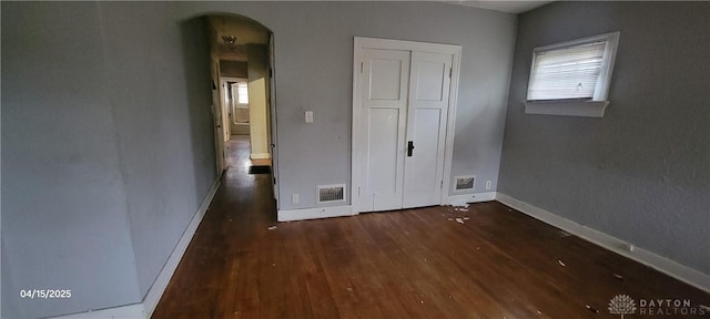 empty room featuring visible vents, baseboards, arched walkways, and wood finished floors
