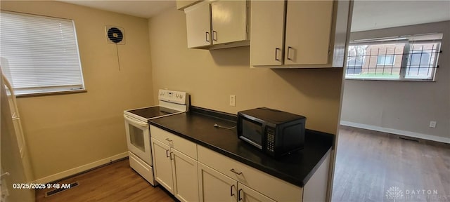 kitchen with white range with electric cooktop, dark countertops, wood finished floors, and black microwave