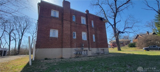 view of side of home featuring a chimney, a yard, and brick siding