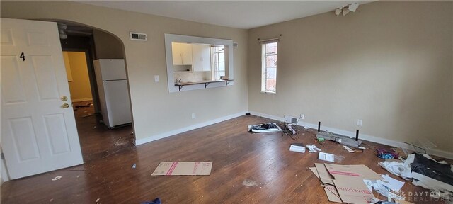 unfurnished dining area with wood finished floors, visible vents, baseboards, and arched walkways