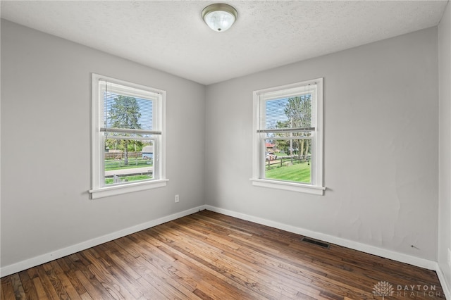 empty room with a textured ceiling, baseboards, visible vents, and hardwood / wood-style flooring