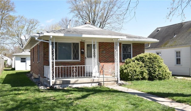 bungalow-style house with brick siding, a porch, a front lawn, and roof with shingles