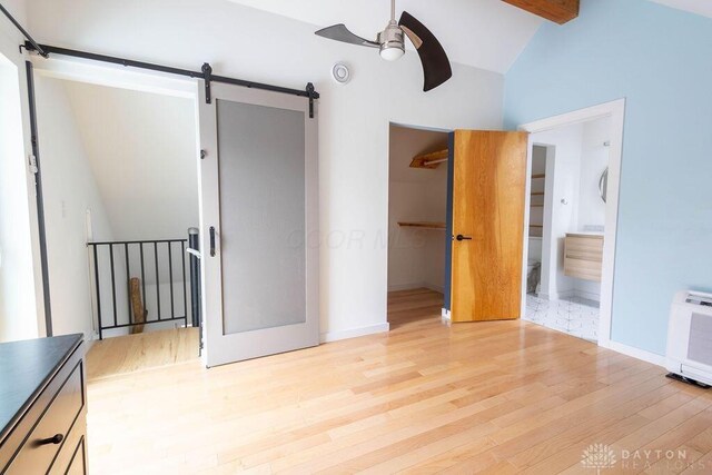 unfurnished bedroom featuring a barn door, vaulted ceiling, wood finished floors, ensuite bathroom, and a spacious closet