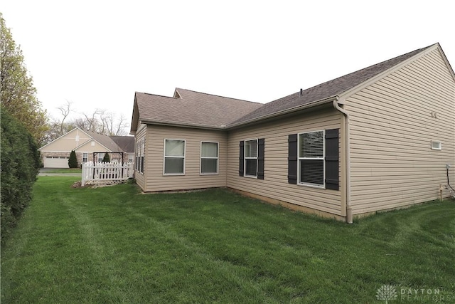 back of house featuring a lawn and a shingled roof