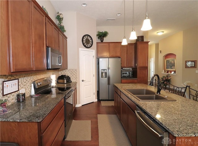 kitchen with a sink, brown cabinets, a kitchen island with sink, appliances with stainless steel finishes, and dark wood-type flooring