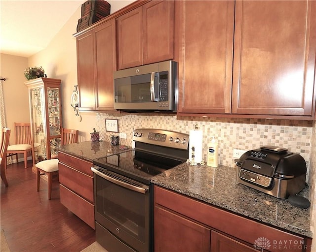 kitchen featuring tasteful backsplash, dark stone countertops, brown cabinetry, appliances with stainless steel finishes, and dark wood-type flooring