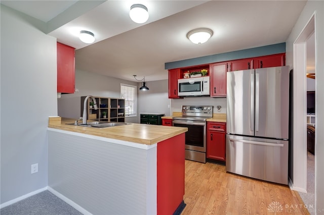 kitchen featuring a peninsula, a sink, light wood-type flooring, light countertops, and appliances with stainless steel finishes
