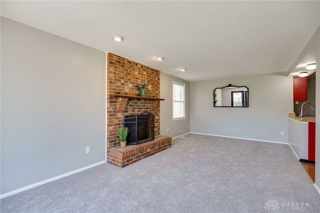 unfurnished living room with baseboards, a brick fireplace, carpet flooring, and a sink