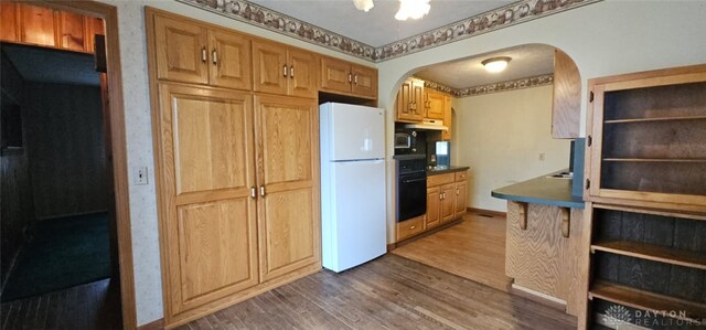 305 S Ada Doty St, Gratis, OH 45330 - kitchen with freestanding refrigerator, arched walkways, dark wood-style flooring, black oven, and under cabinet range hood