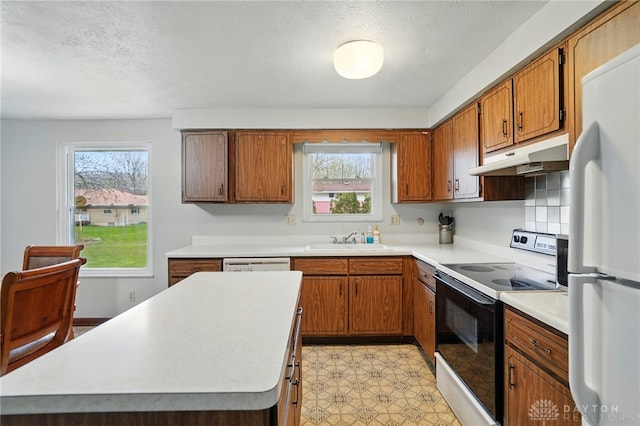 kitchen featuring a sink, brown cabinetry, white appliances, light countertops, and under cabinet range hood
