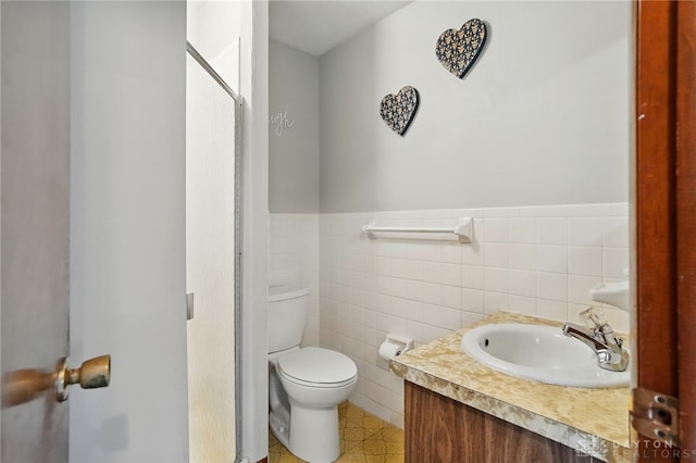 bathroom with vanity, toilet, a wainscoted wall, and tile walls