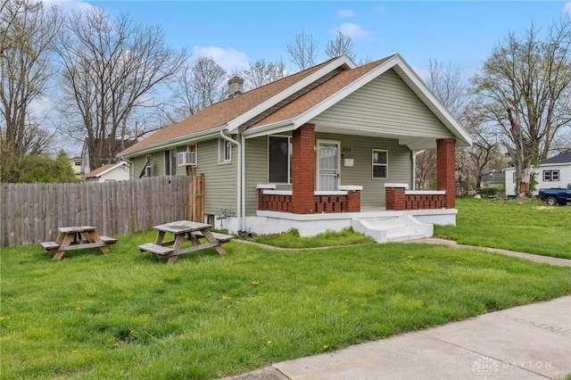 bungalow-style house featuring a chimney, fence, a porch, a front yard, and roof with shingles