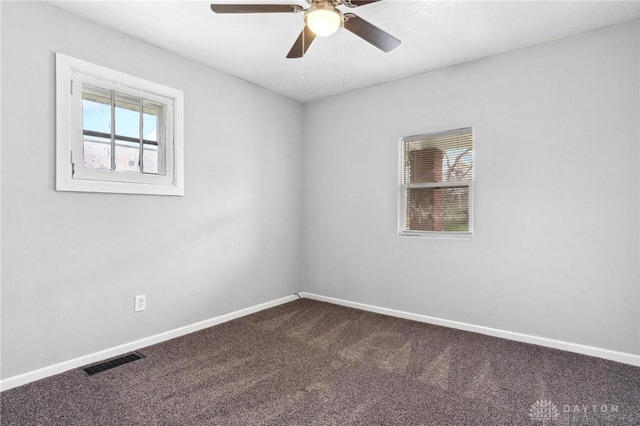 spare room with a ceiling fan, a healthy amount of sunlight, dark colored carpet, and visible vents