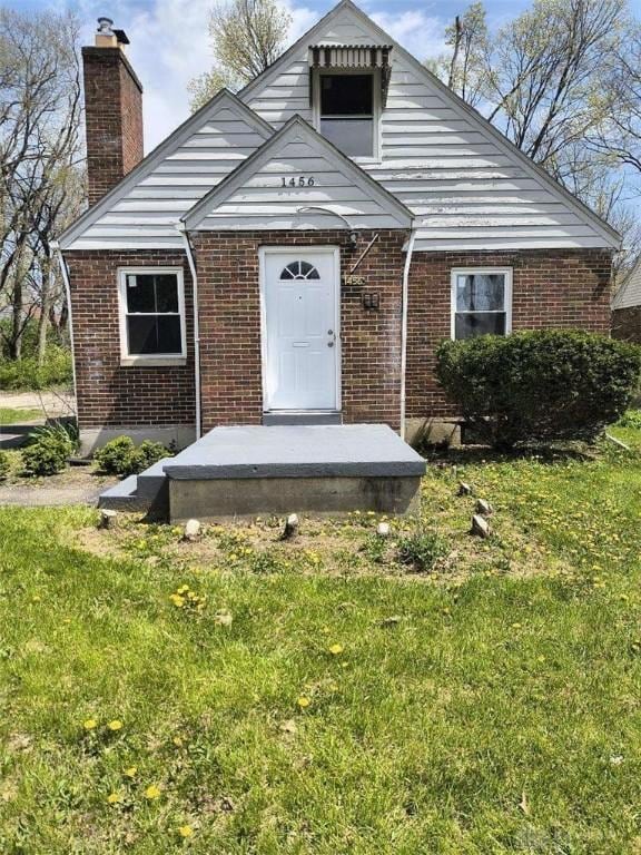 view of front of house with brick siding, a chimney, and a front lawn