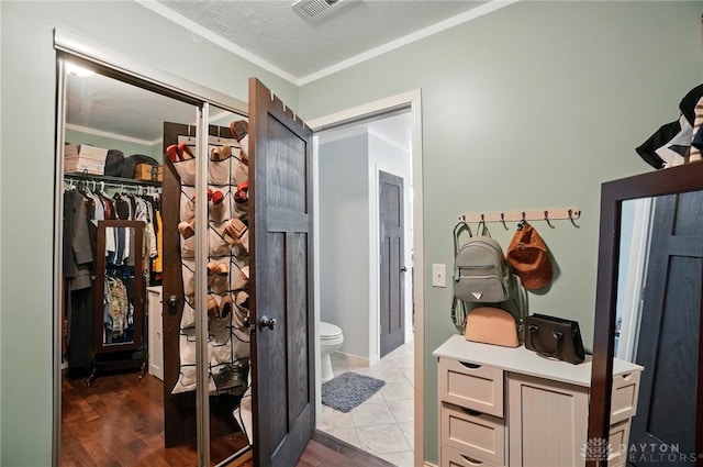 bathroom with wood finished floors, a textured ceiling, a walk in closet, toilet, and visible vents