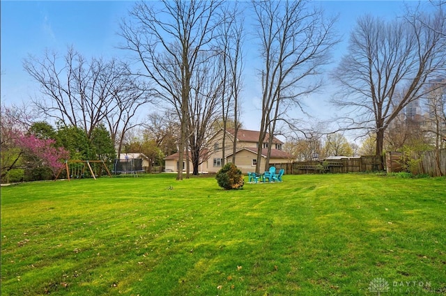 view of yard featuring fence, a trampoline, and a playground
