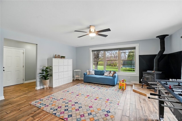 interior space featuring hardwood / wood-style flooring, ceiling fan, baseboards, and a wood stove