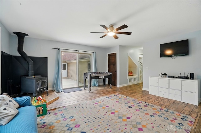 living area with wood finished floors, stairs, ceiling fan, a wood stove, and baseboards