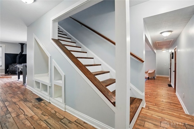 stairway with hardwood / wood-style flooring, baseboards, a wood stove, and visible vents