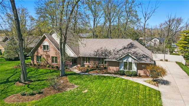 view of front of house featuring a front lawn, driveway, fence, brick siding, and roof with shingles