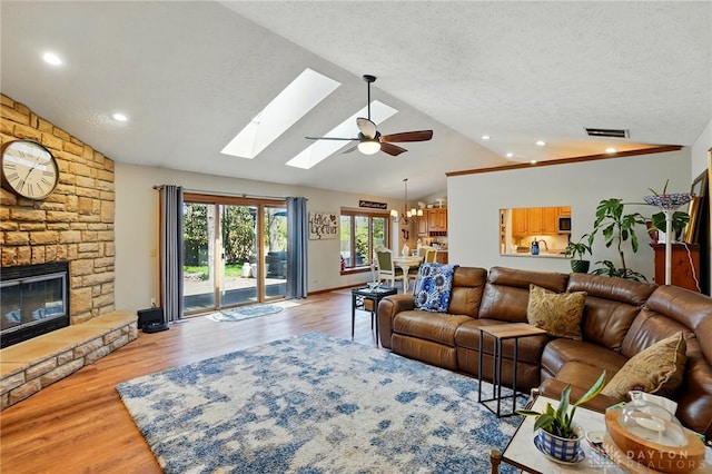 living room featuring light wood finished floors, visible vents, vaulted ceiling with skylight, ceiling fan with notable chandelier, and a fireplace