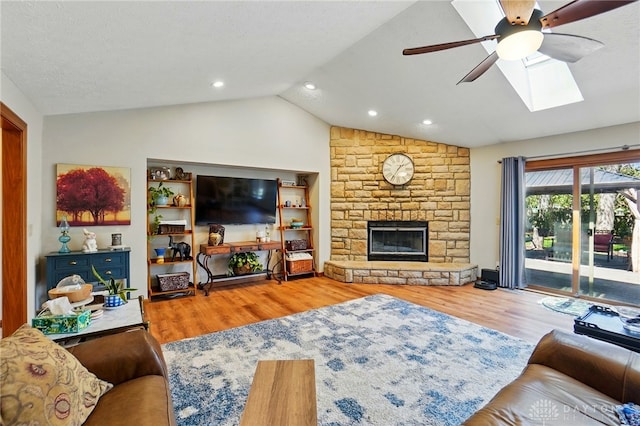 living area featuring lofted ceiling with skylight, recessed lighting, wood finished floors, ceiling fan, and a stone fireplace