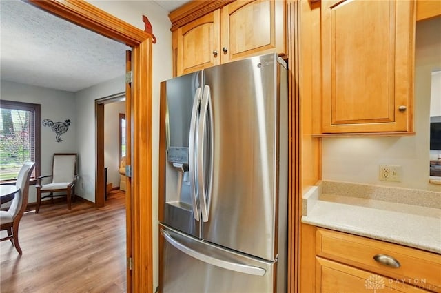 kitchen with light wood finished floors, a textured ceiling, stainless steel fridge with ice dispenser, brown cabinetry, and light countertops