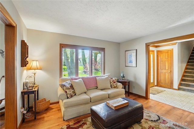 living area featuring light wood-type flooring, baseboards, a textured ceiling, and stairway