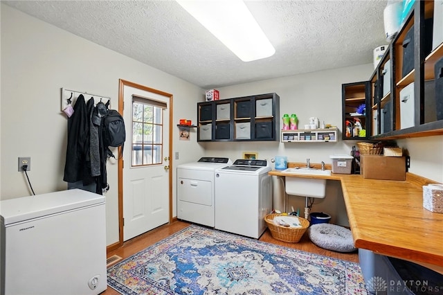 washroom with laundry area, wood finished floors, a sink, independent washer and dryer, and a textured ceiling