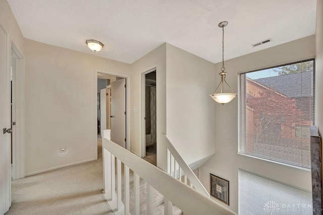 hall featuring baseboards, visible vents, carpet floors, and an upstairs landing