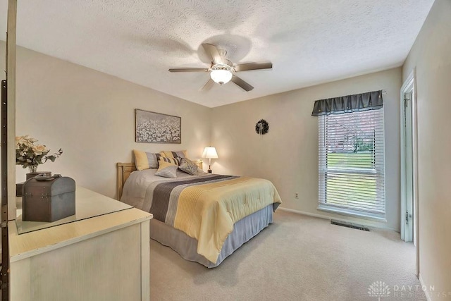 bedroom featuring a textured ceiling, ceiling fan, light colored carpet, baseboards, and visible vents