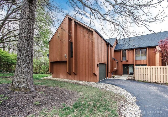 view of front of home with an attached garage, a shingled roof, fence, and aphalt driveway